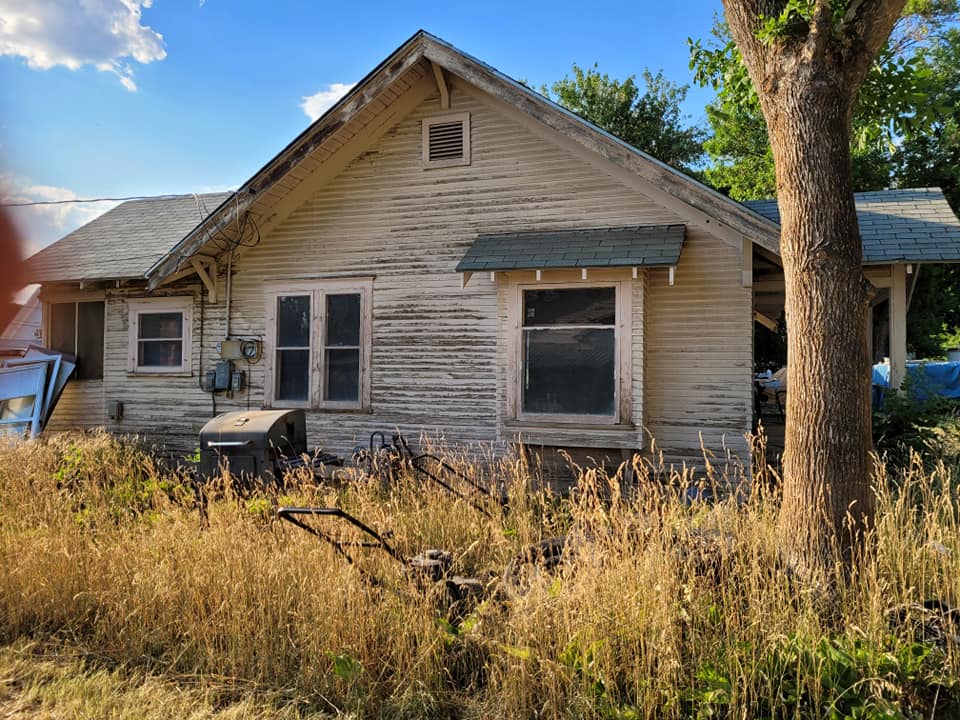 First project house before restoration, with weathered siding and an overgrown yard